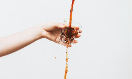 A picture of coffee being poured into a cup and overflowing while someone is holding the cup